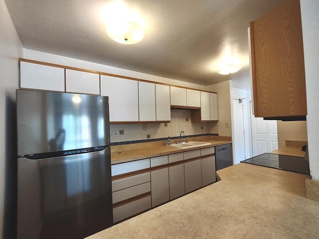 kitchen with freestanding refrigerator, a sink, tasteful backsplash, white cabinets, and dishwashing machine