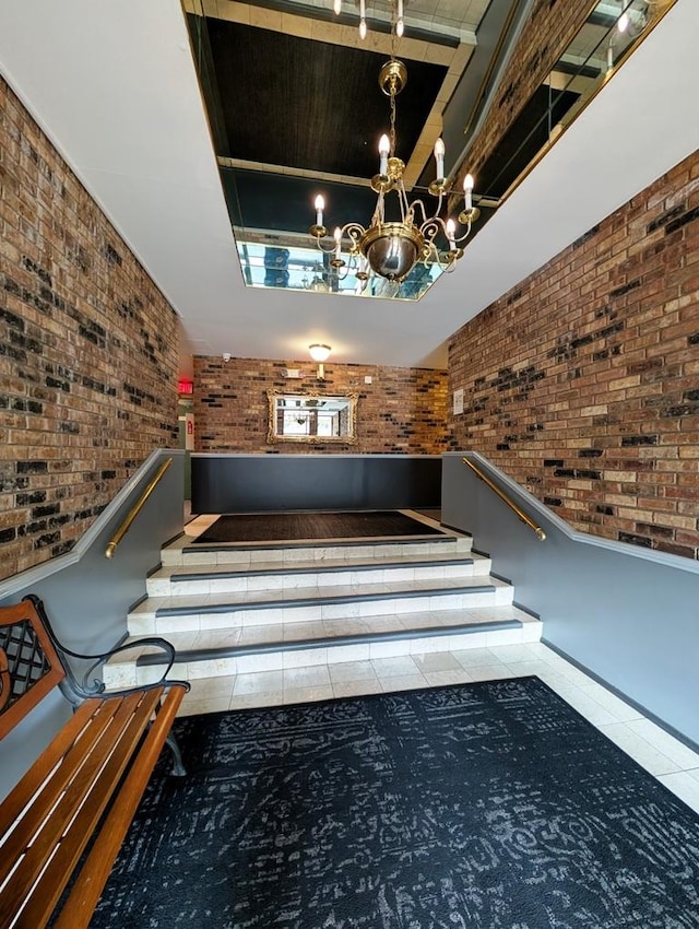 staircase featuring brick wall, tile patterned floors, a tray ceiling, and a chandelier