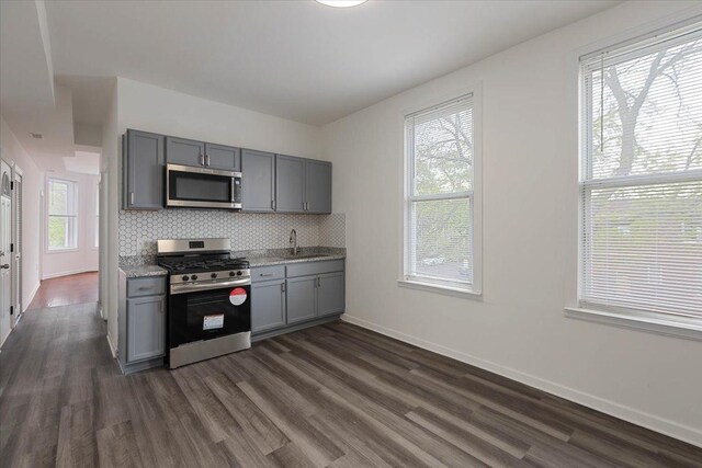 kitchen featuring gray cabinetry, a healthy amount of sunlight, stainless steel appliances, and dark wood-type flooring