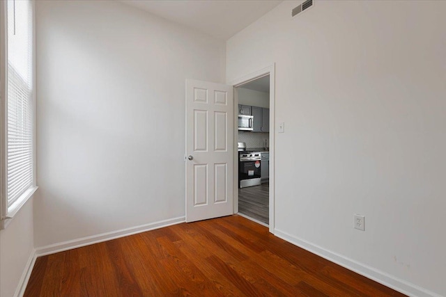 unfurnished room with visible vents, dark wood-style flooring, and baseboards