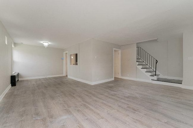 unfurnished living room featuring baseboards, stairway, and wood finished floors