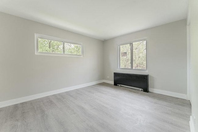 unfurnished room featuring baseboards, radiator heating unit, and wood finished floors