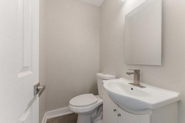 half bath featuring baseboards, toilet, and vanity