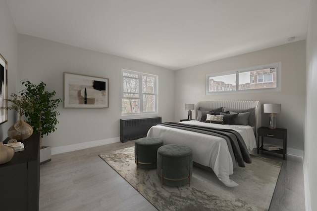 bedroom featuring baseboards, radiator heating unit, and light wood-type flooring