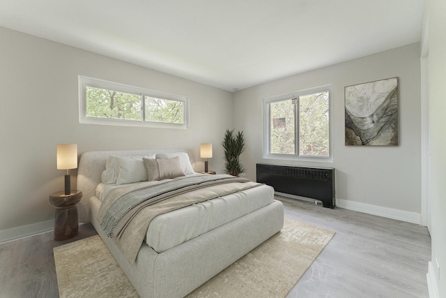 bedroom with baseboards, radiator heating unit, and light wood-type flooring