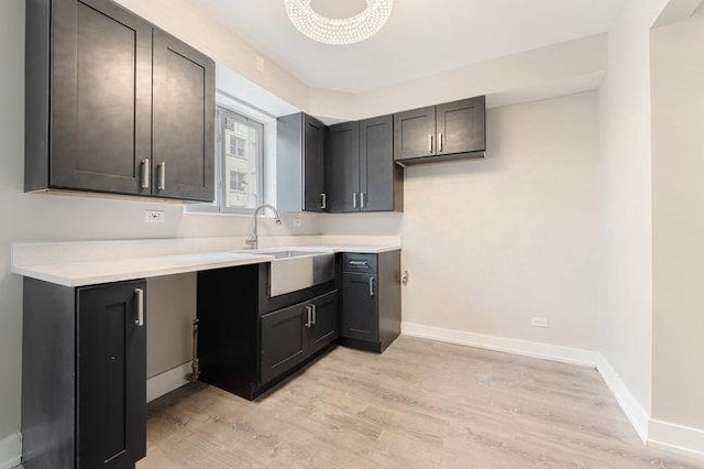 kitchen featuring baseboards, light countertops, light wood-style flooring, and a sink