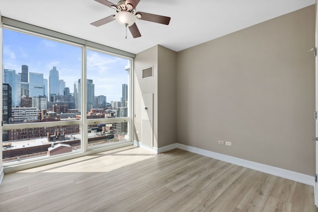spare room with visible vents, a view of city, wood finished floors, ceiling fan, and expansive windows
