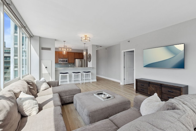 living room featuring baseboards, a chandelier, visible vents, and light wood-style floors