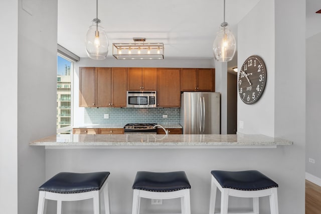 kitchen with appliances with stainless steel finishes, brown cabinetry, backsplash, and a peninsula
