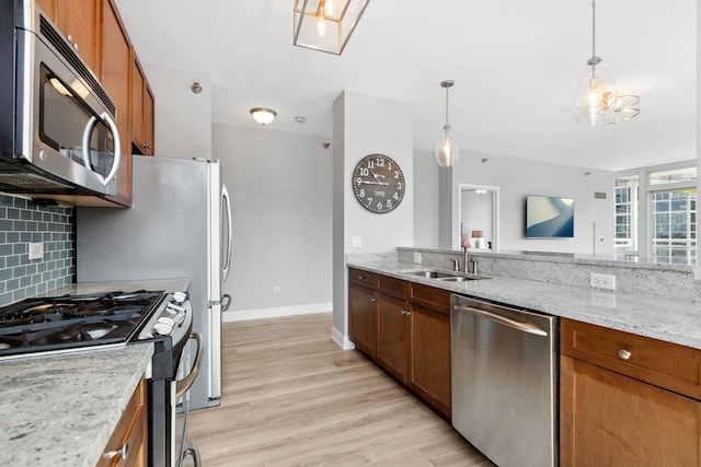 kitchen with appliances with stainless steel finishes, tasteful backsplash, a sink, brown cabinetry, and light wood-type flooring