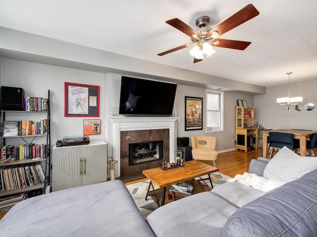 living room with a fireplace, wood finished floors, ceiling fan, a chandelier, and baseboards