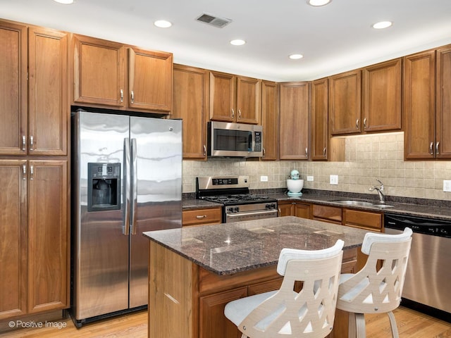 kitchen featuring stainless steel appliances, a sink, a center island, dark stone counters, and a kitchen breakfast bar
