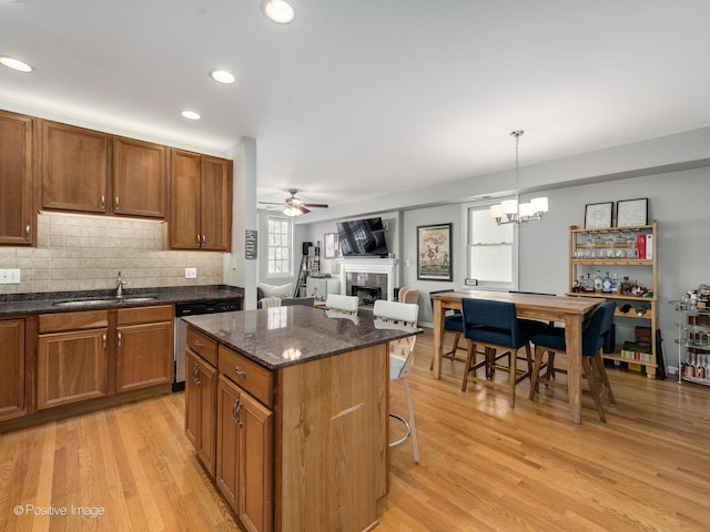 kitchen featuring a sink, dishwasher, a tile fireplace, light wood-type flooring, and brown cabinetry