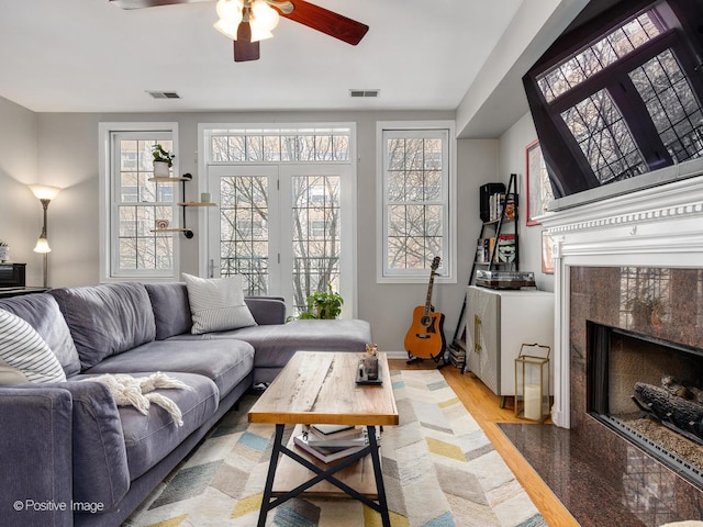 living room featuring a ceiling fan, plenty of natural light, a high end fireplace, and light wood-style floors