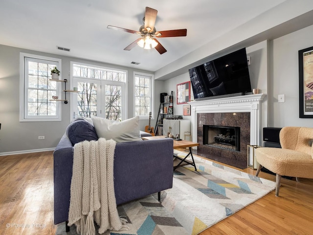 living room featuring wood finished floors, a ceiling fan, a fireplace, and healthy amount of natural light