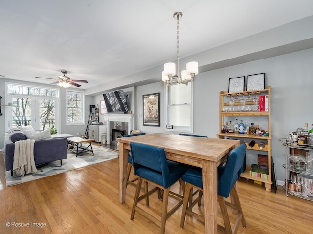 dining area with light wood-style flooring, a chandelier, a fireplace, and a ceiling fan