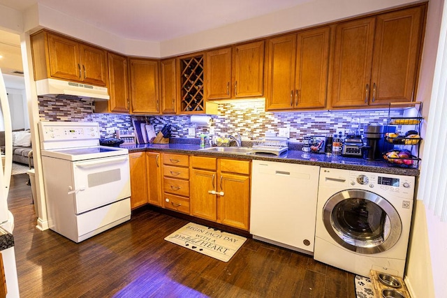 kitchen featuring washer / clothes dryer, dark countertops, a sink, under cabinet range hood, and white appliances