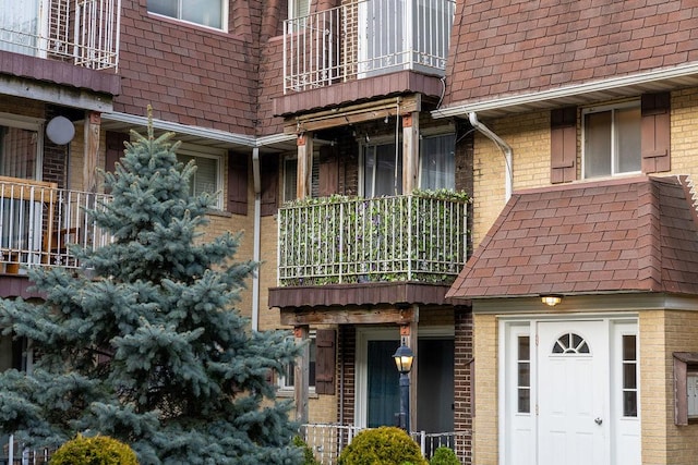 doorway to property featuring brick siding, a shingled roof, and a balcony