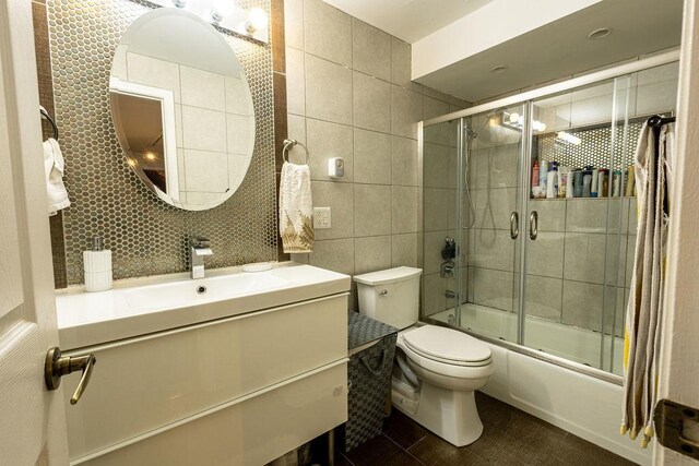 full bathroom with vanity, toilet, tile walls, tile patterned floors, and combined bath / shower with glass door