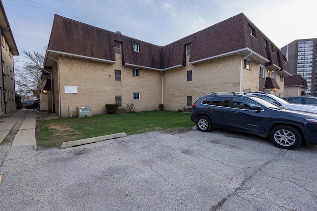 view of side of property with roof with shingles, mansard roof, uncovered parking, and brick siding