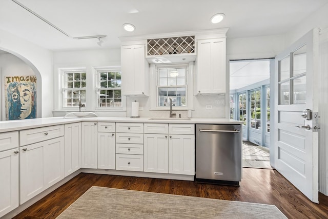 kitchen featuring stainless steel dishwasher, light countertops, arched walkways, white cabinets, and a sink