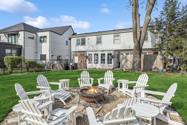 rear view of property with a lawn, a fire pit, and fence