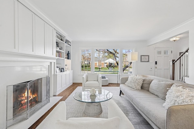 living area with crown molding, a warm lit fireplace, stairs, baseboards, and wood finished floors