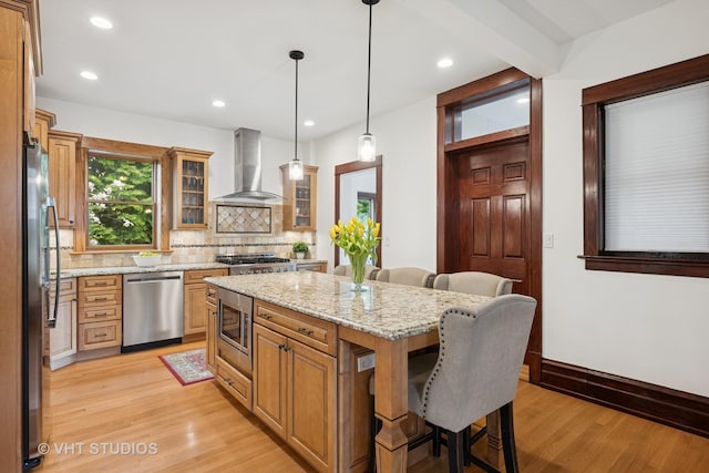 1625 Central Ave, Wilmette, IL 60091 - kitchen featuring appliances with stainless steel finishes, light wood-style flooring, wall chimney exhaust hood, tasteful backsplash, and a kitchen bar