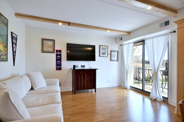 living area featuring baseboards, beamed ceiling, light wood finished floors, and visible vents