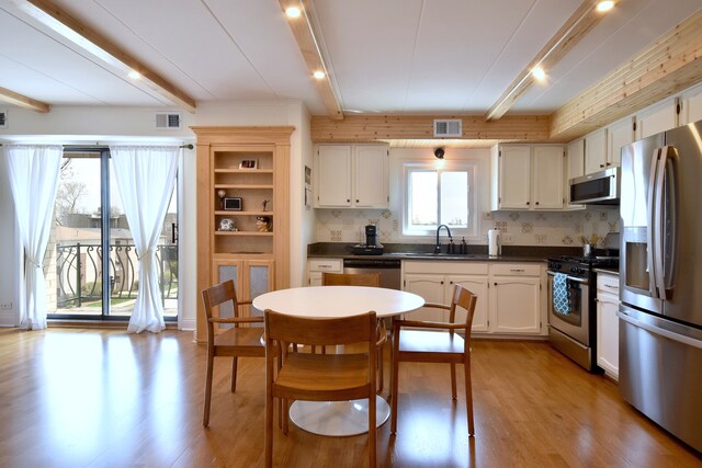 kitchen featuring visible vents, beam ceiling, dark countertops, a sink, and stainless steel appliances
