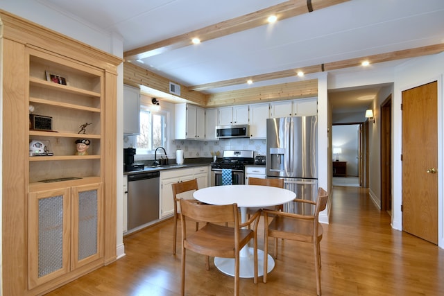 kitchen featuring appliances with stainless steel finishes, tasteful backsplash, beam ceiling, a sink, and light wood-style floors