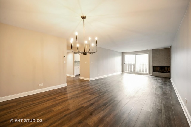 unfurnished living room featuring a brick fireplace, baseboards, a notable chandelier, and dark wood finished floors