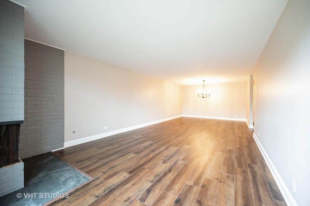 unfurnished living room featuring baseboards, a chandelier, wood finished floors, and a fireplace