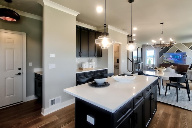 kitchen with crown molding, a kitchen island, light countertops, visible vents, and dark wood-type flooring