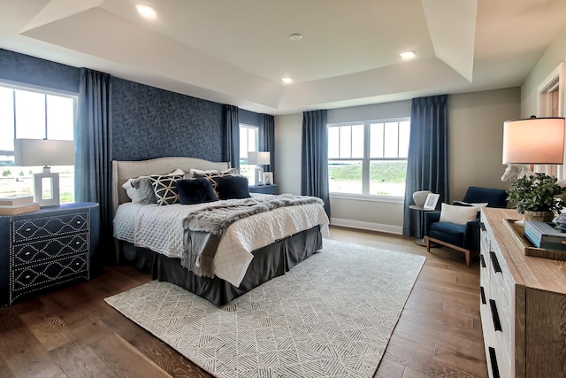 bedroom with recessed lighting, baseboards, wood finished floors, and a tray ceiling
