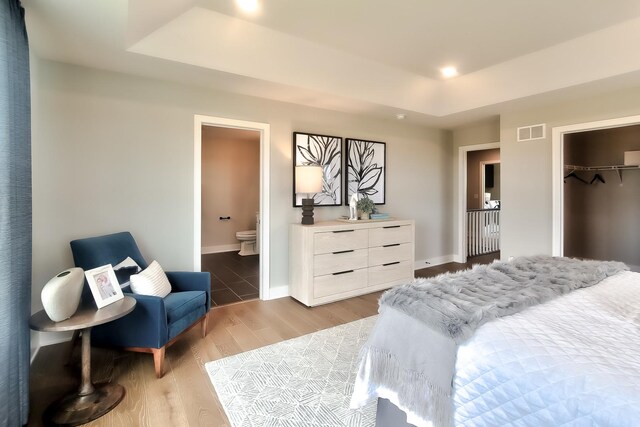 bedroom with a raised ceiling, visible vents, light wood-style floors, a closet, and baseboards