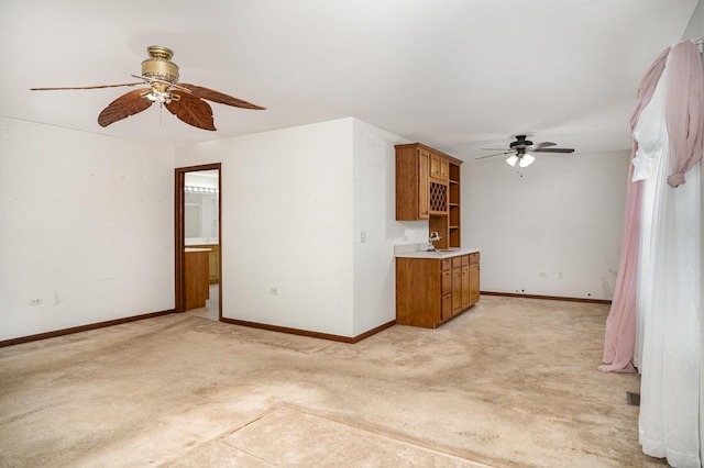 unfurnished living room featuring a sink, baseboards, light carpet, and a ceiling fan