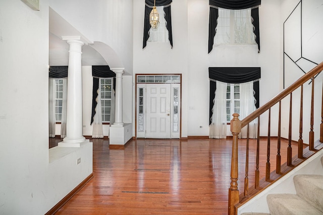 entryway with a high ceiling, arched walkways, decorative columns, wood finished floors, and stairway