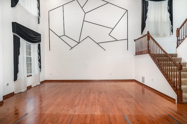 unfurnished living room with baseboards, visible vents, stairway, and hardwood / wood-style floors