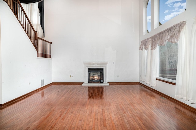 unfurnished living room with stairway, baseboards, a glass covered fireplace, a high ceiling, and hardwood / wood-style floors