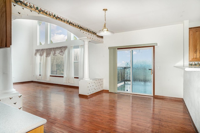 unfurnished dining area featuring baseboards, decorative columns, and wood finished floors