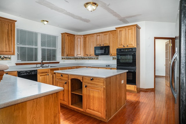 kitchen with a center island, a sink, light countertops, black appliances, and light wood-style flooring