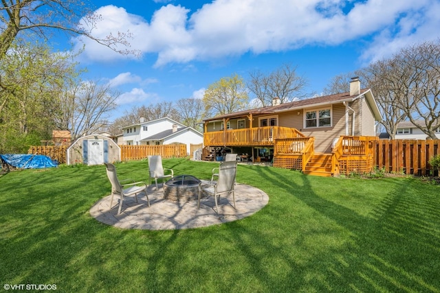 rear view of property with fence private yard, a deck, a chimney, a storage unit, and an outdoor fire pit