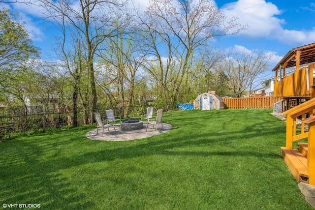 view of yard featuring a storage unit, a fenced backyard, an outbuilding, a patio, and a fire pit