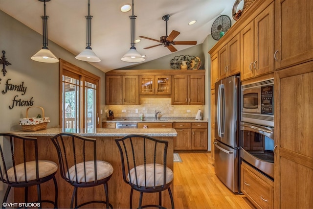 kitchen featuring brown cabinetry, stainless steel appliances, decorative backsplash, a kitchen bar, and vaulted ceiling