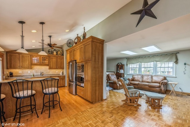 kitchen featuring appliances with stainless steel finishes, a kitchen breakfast bar, brown cabinetry, decorative backsplash, and a skylight