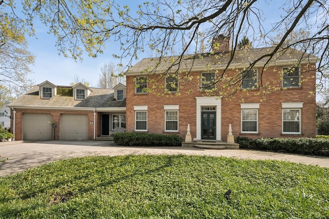 colonial inspired home featuring a chimney, driveway, brick siding, a garage, and a front lawn