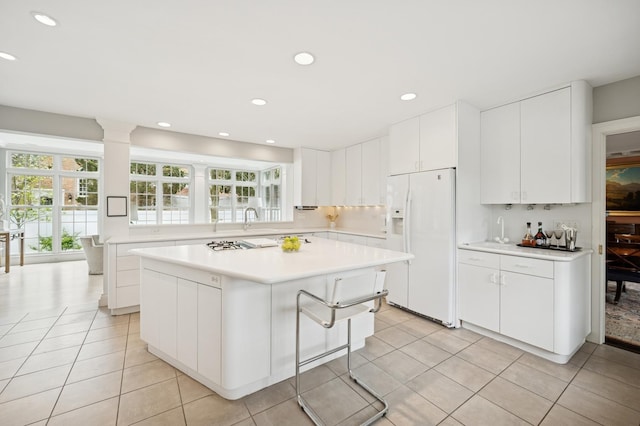 kitchen with white fridge with ice dispenser, a center island, light tile patterned floors, light countertops, and white cabinets