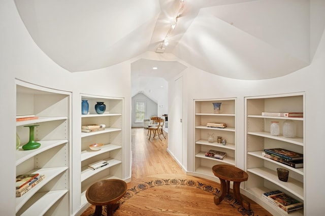 corridor featuring rail lighting, light wood-style floors, built in features, and vaulted ceiling