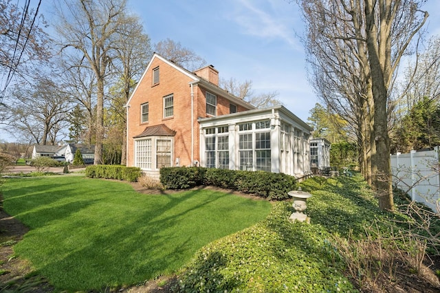 view of property exterior featuring a sunroom, a yard, a chimney, fence, and brick siding